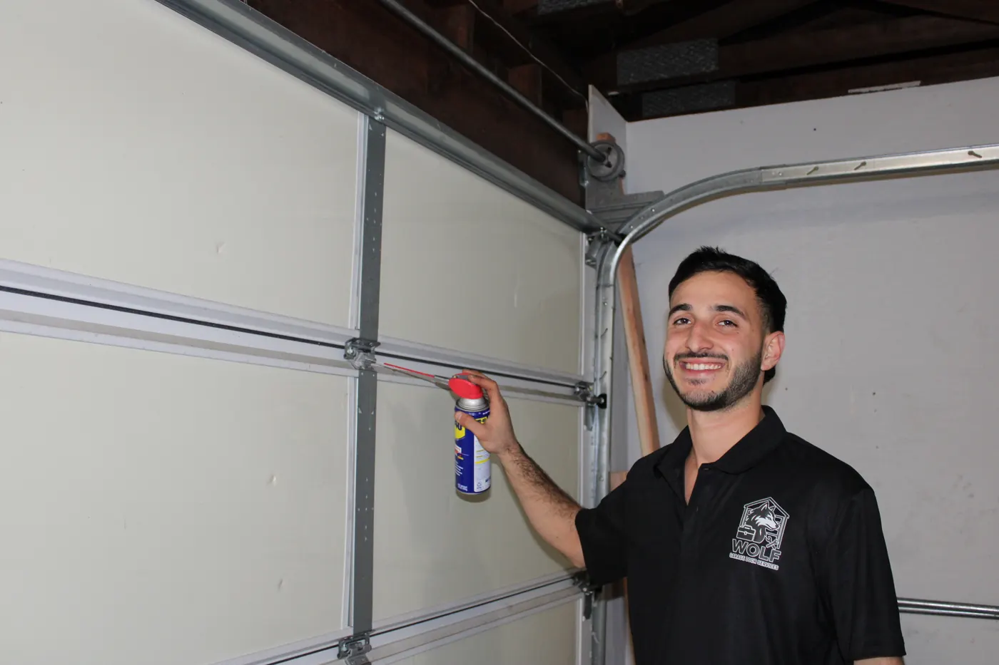 Smiling Wolf technician lubricating garage door hardware during maintenance