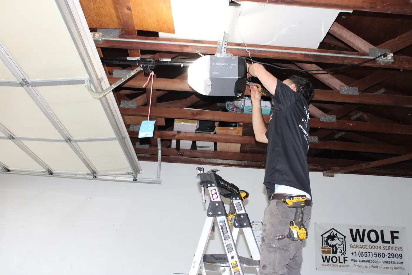 Technician mounting a ceiling garage door opener from a ladder